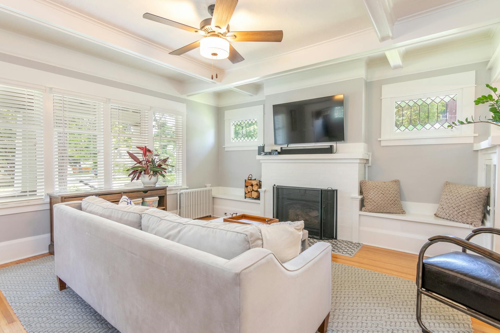 Living room with a white couch, fireplace, and large window with shutters.