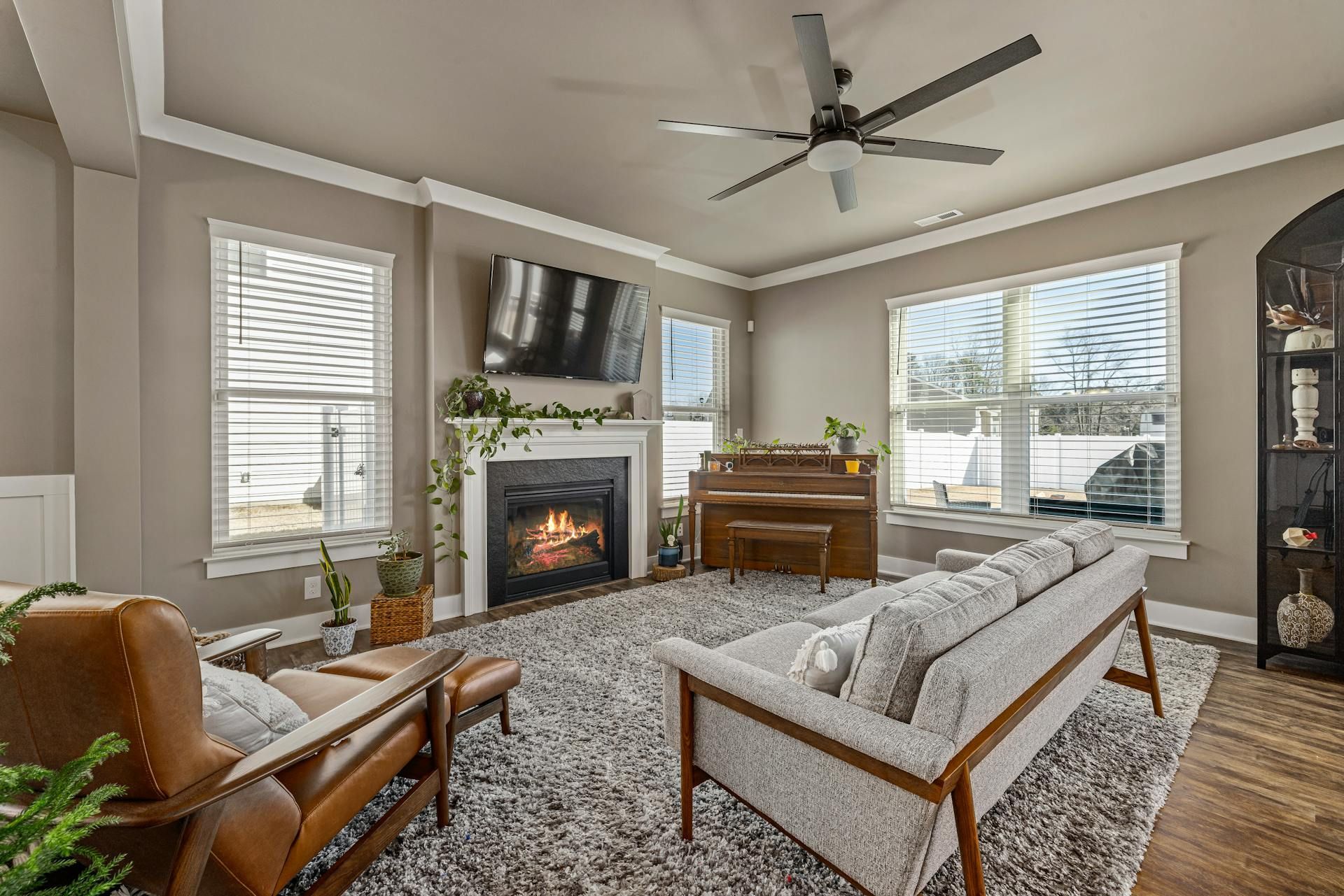 Living room with a fireplace, piano, and modern furniture; a ceiling fan is visible.