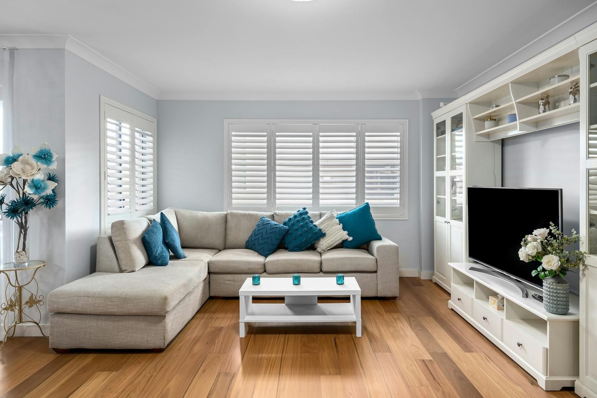 Living room with light-colored walls, sectional sofa with blue pillows, built-in entertainment center, and wooden floors.