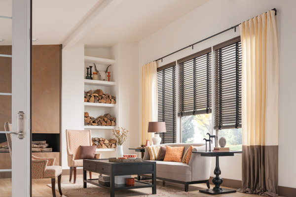 Living room with dark wood blinds, beige curtains, and a built-in shelf with firewood.