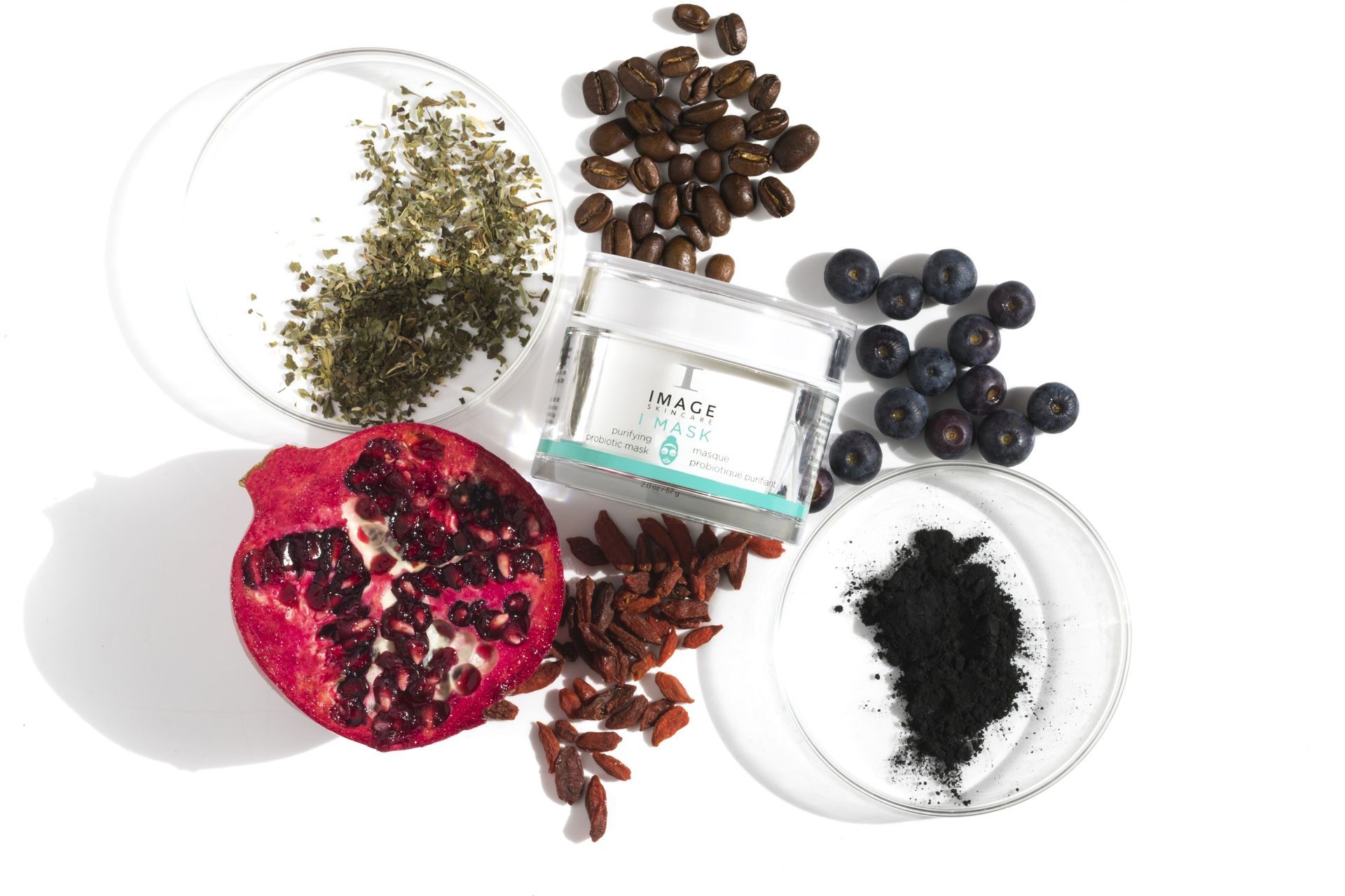 Cream jar surrounded by ingredients like pomegranate, coffee beans, blueberries, goji berries, and herbs.
