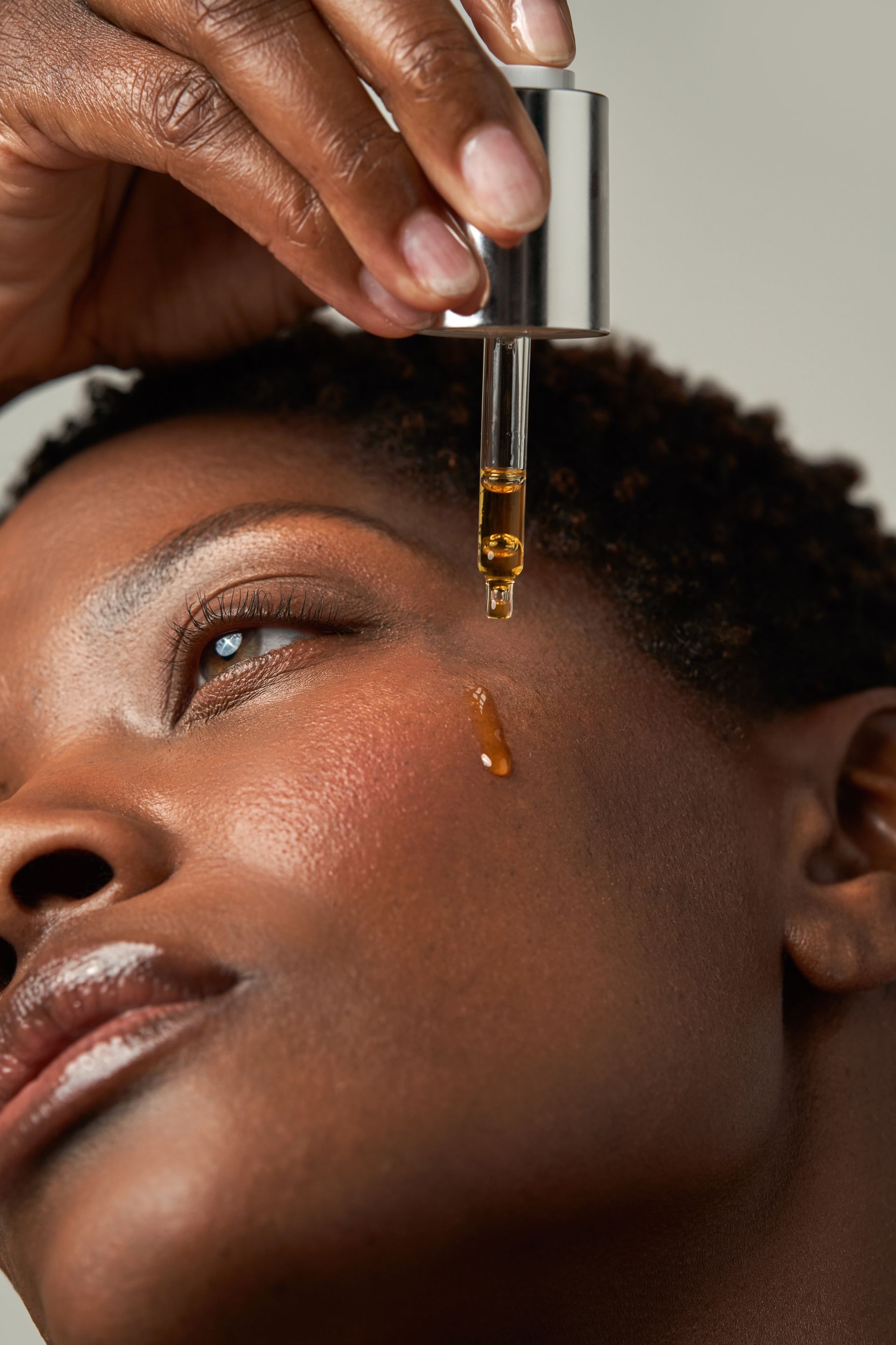 Woman applying face serum with a dropper; close-up shot with dewy skin.