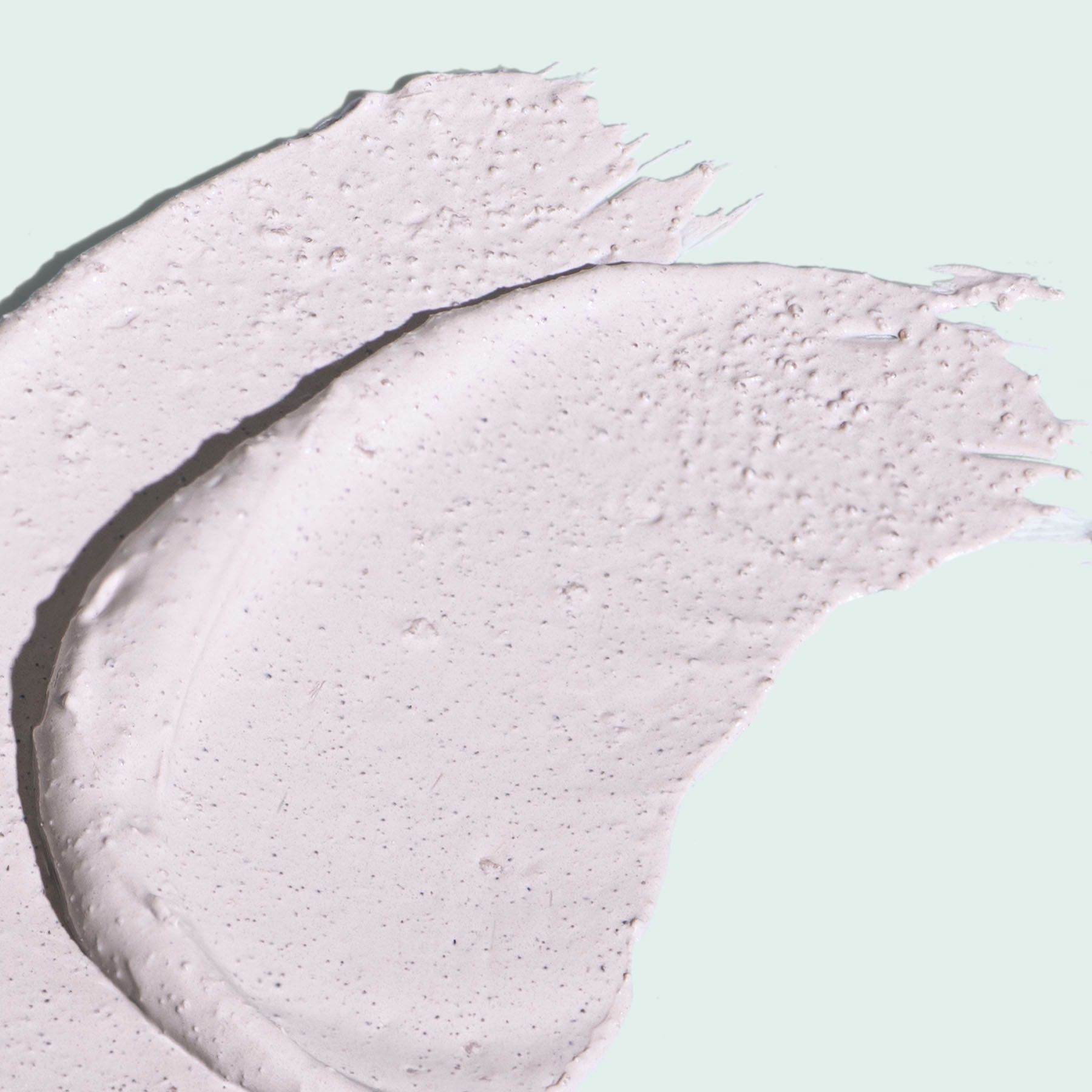 Swatches of light lavender-colored cream, likely a cosmetic product, on a light blue-green surface.