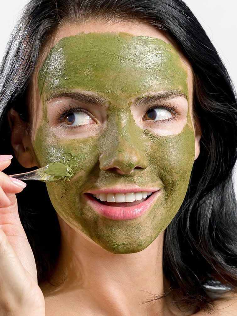 Woman applying green facial mask, smiling, close-up.