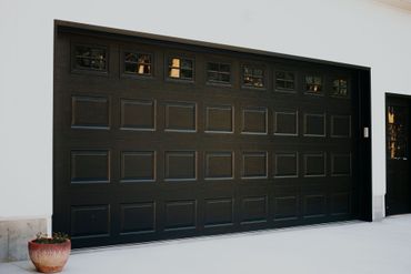 Black garage door with small windows in a white wall, seen from a snowy driveway