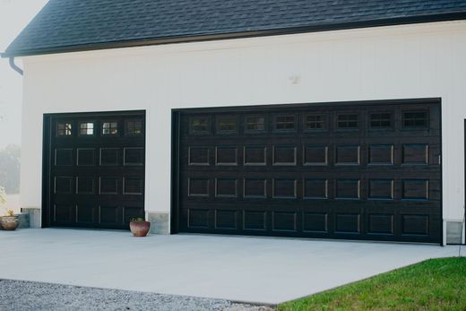 White house exterior with two black garage doors and a small potted plant by the driveway