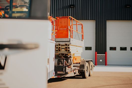 Orange cherry picker parked outside a warehouse, with white garage doors in the background.