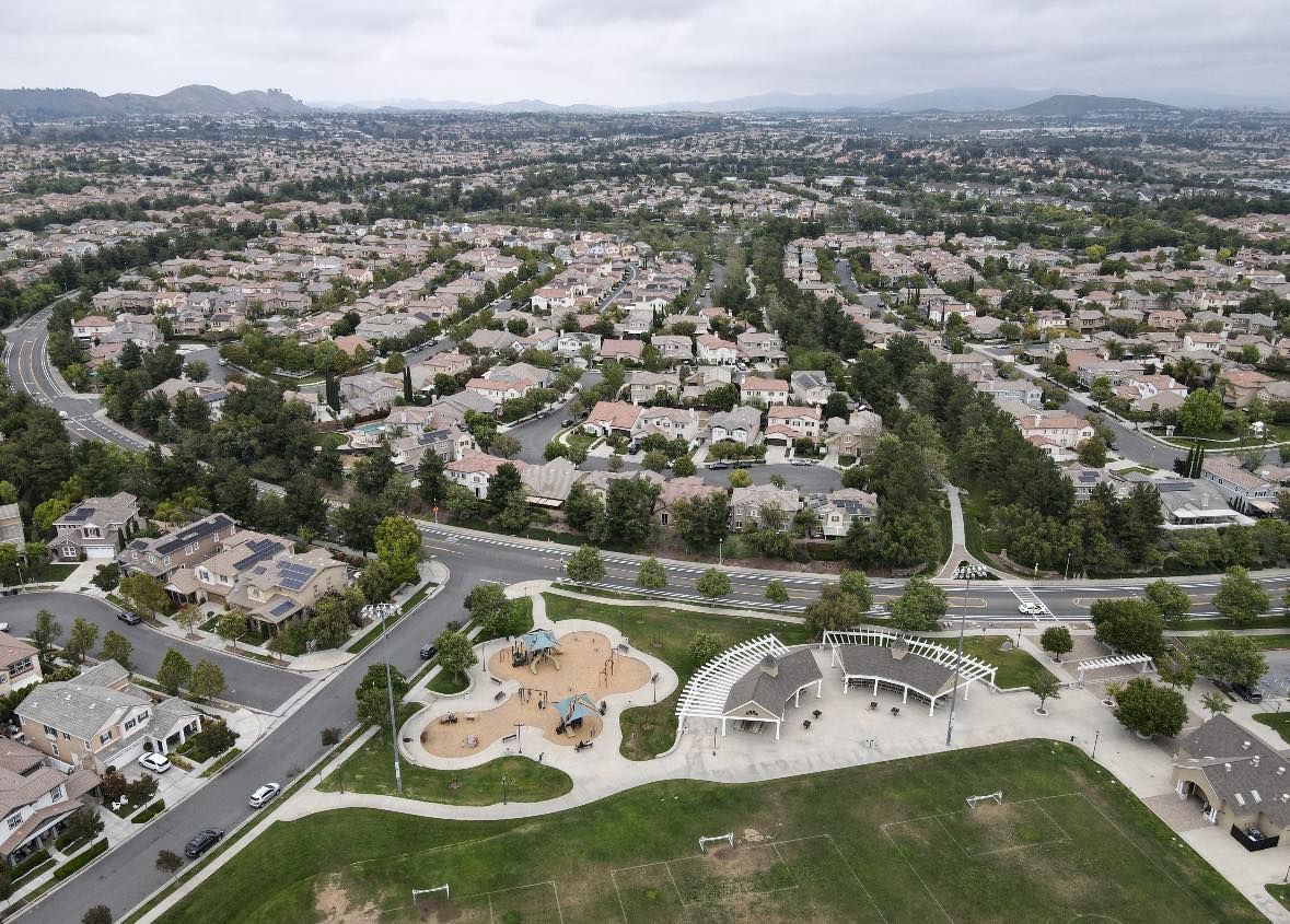 Aerial view of a sprawling suburban Harveston neighborhood with houses, roads, and a park playground in the foreground