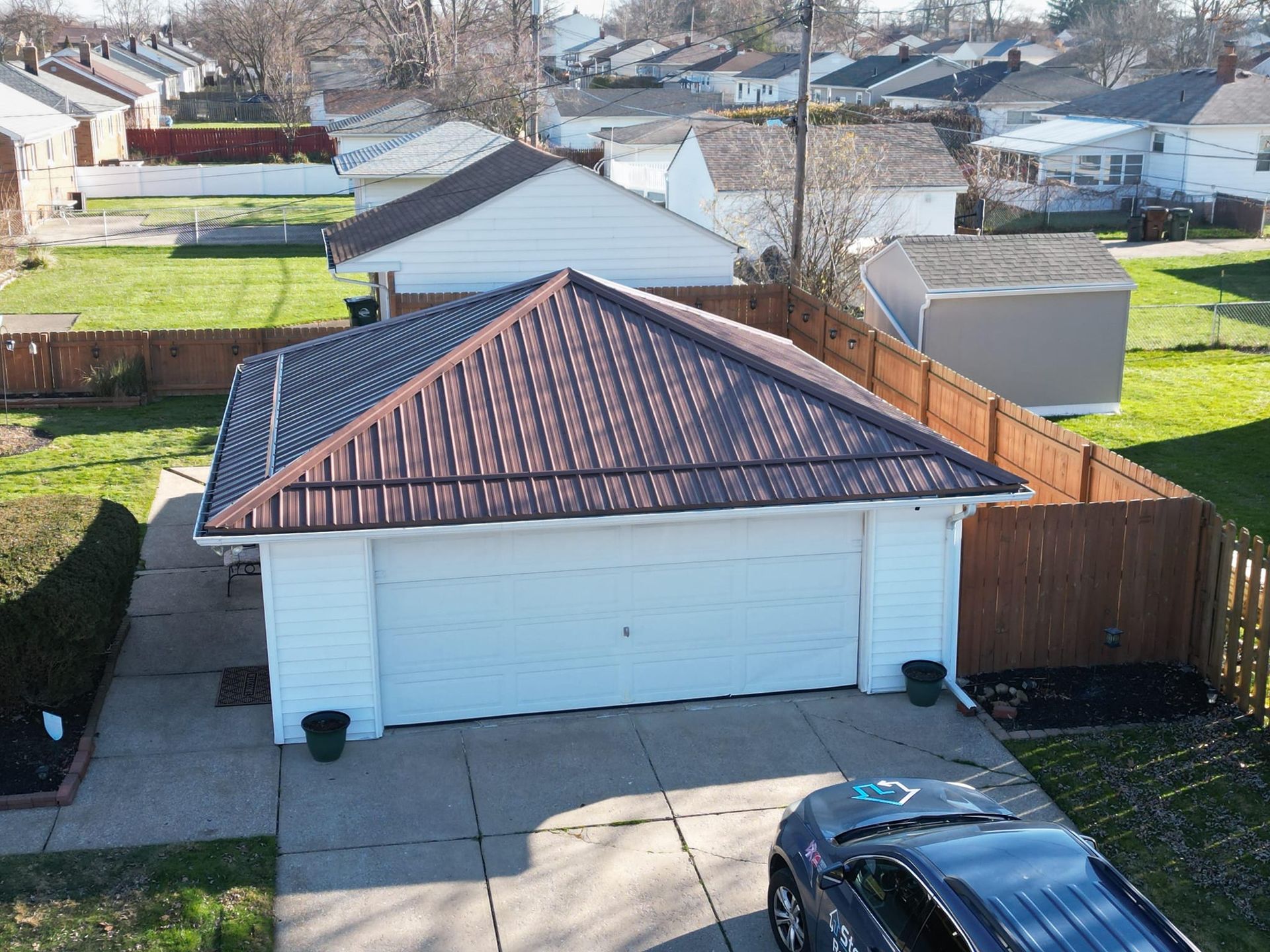 A white garage with a brown metal roof in a residential neighborhood. A car is parked in the driveway.