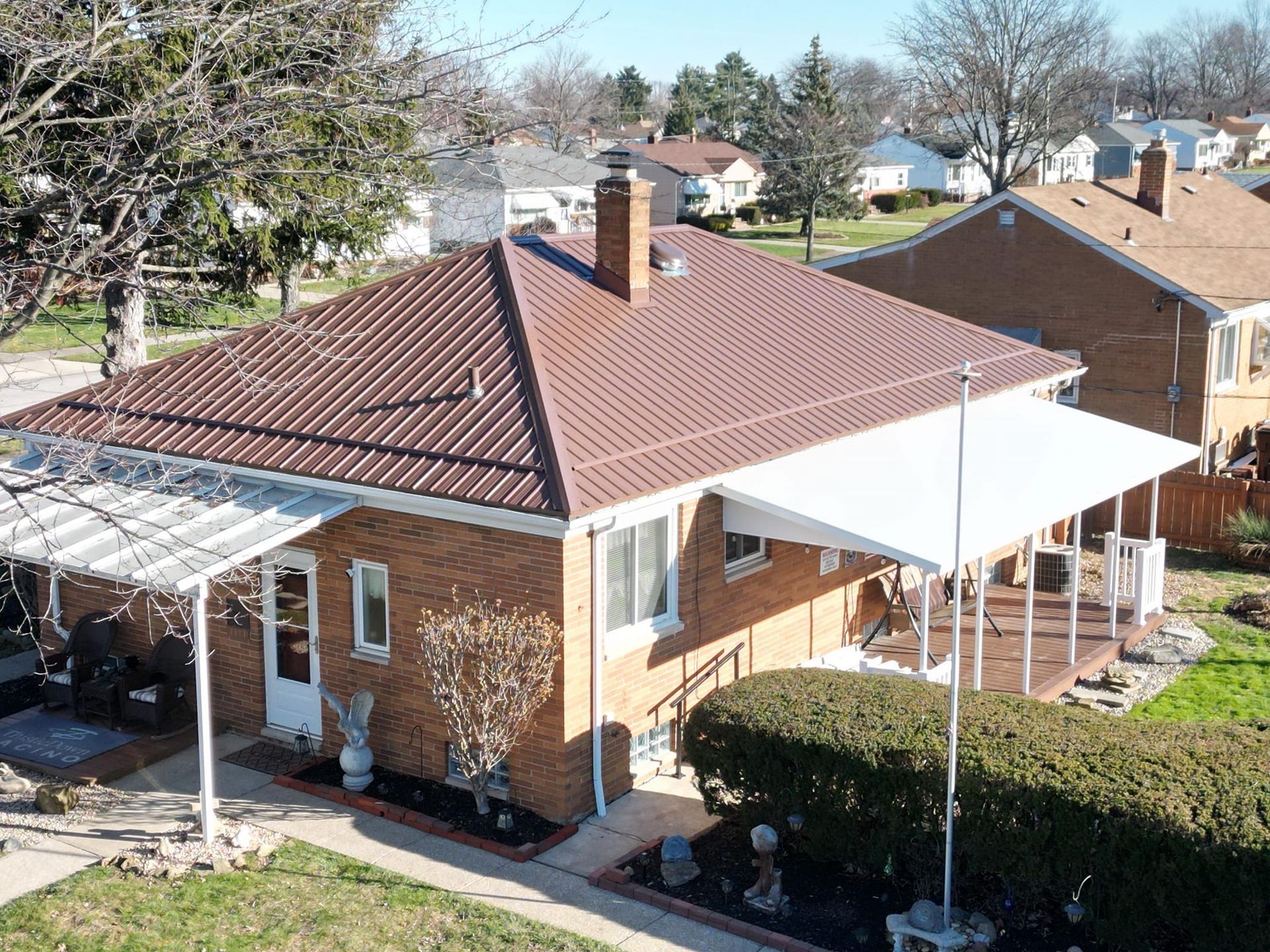 Brick house with a brown corrugated metal roof, covered patios, and a deck in a suburban setting.