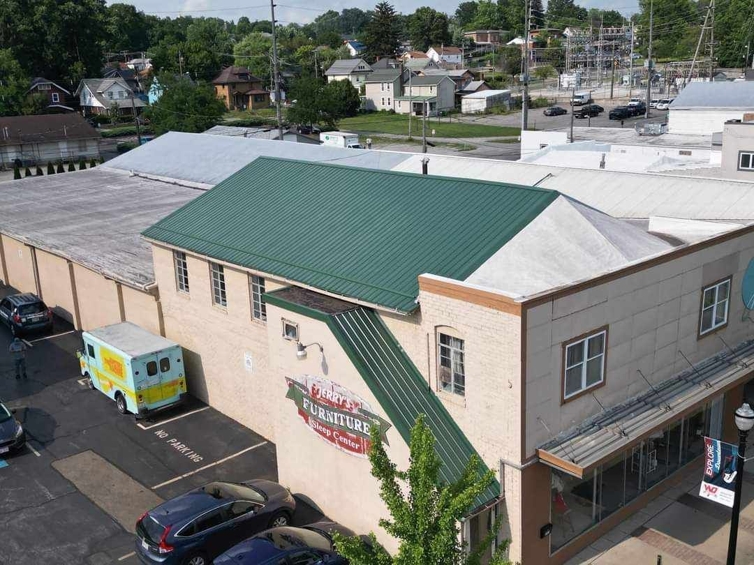 An aerial view of a building with a green roof and a mural, with cars parked on the street. A food truck is also visible.