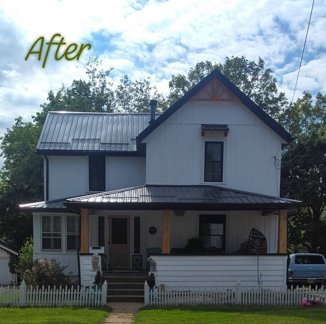 White two-story house with a black metal roof, porch, and a white picket fence. The 