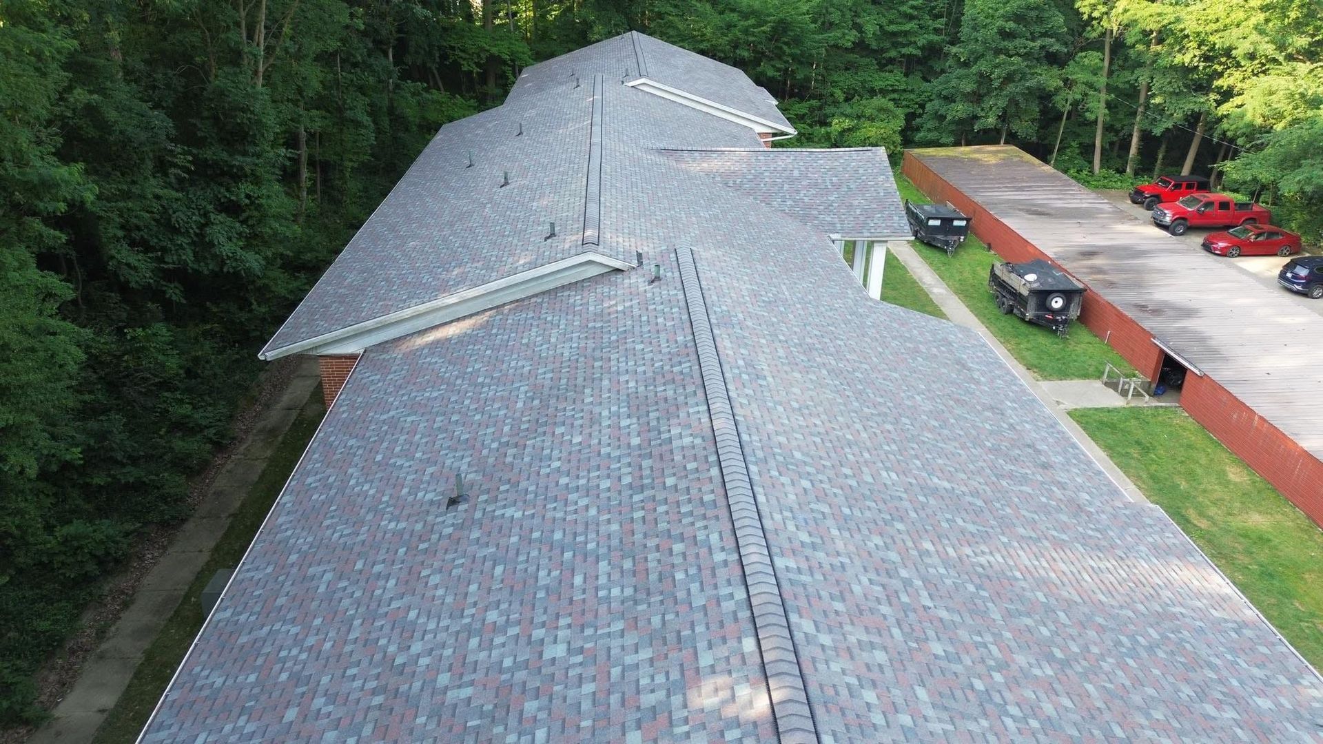 Aerial view of a multi-sectioned building with a gray shingled roof surrounded by trees. 
