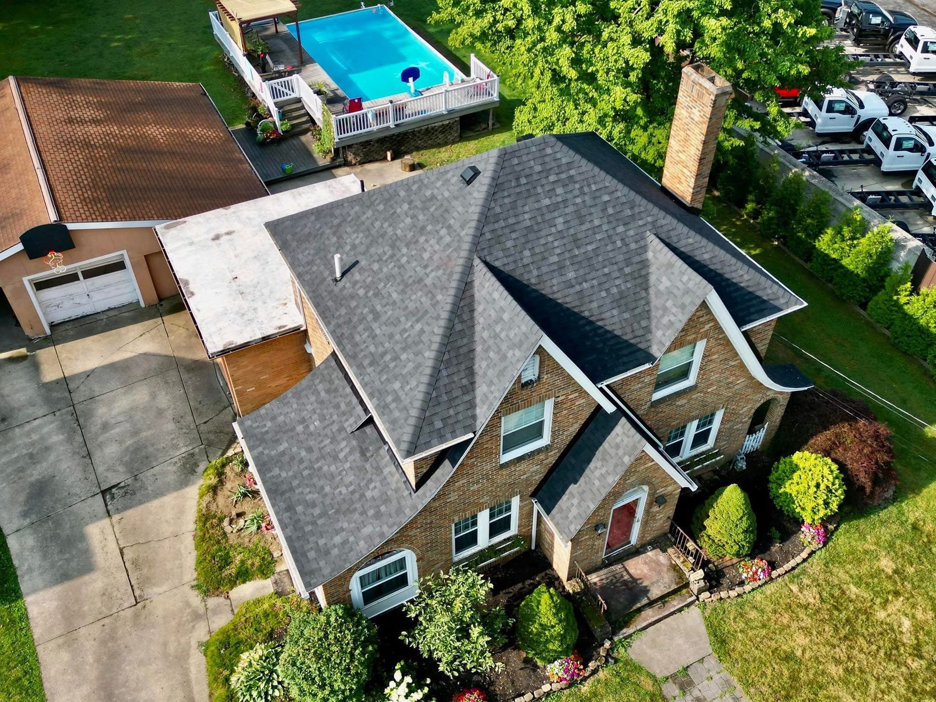 Overhead view of a two-story house with a dark gray roof, a garage, and a backyard with a pool.