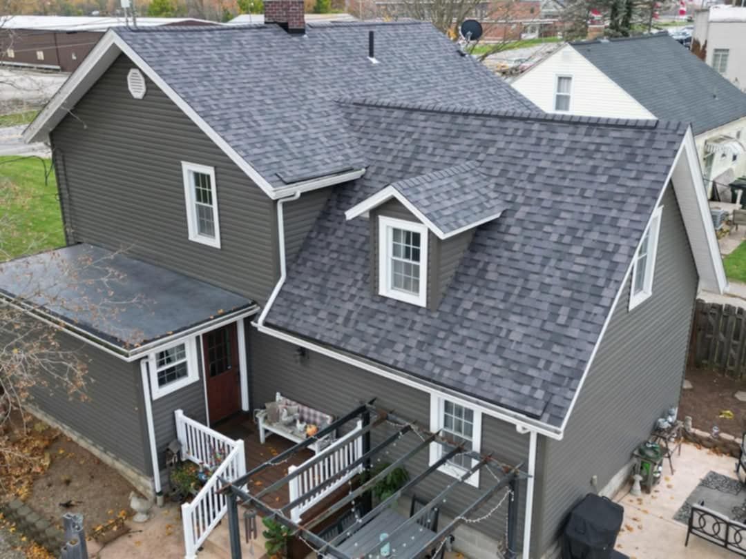 Gray house with a dark gray shingle roof, white trim, and a small dormer. A patio and deck are visible.
