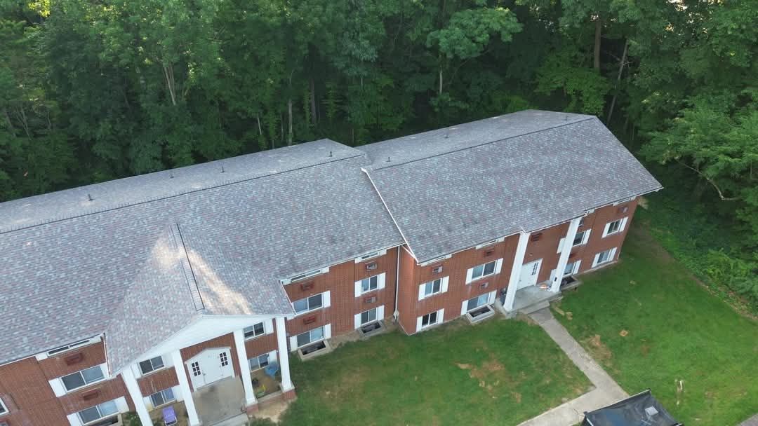 Aerial view of a two-story brick apartment building with a gray roof, surrounded by green grass and trees.