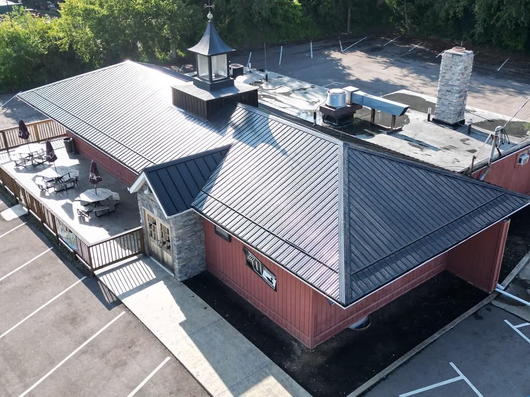 Aerial view of a red building with a black metal roof and a wooden outdoor seating area.