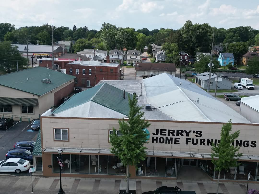 An aerial view of Jerry's Home Furnishings, a beige building with a green roof, in a town with trees and houses.