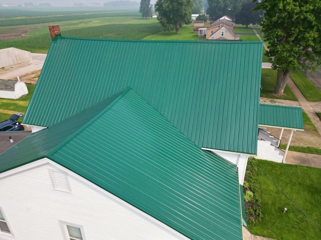 Green metal roof on a white house in a rural setting.