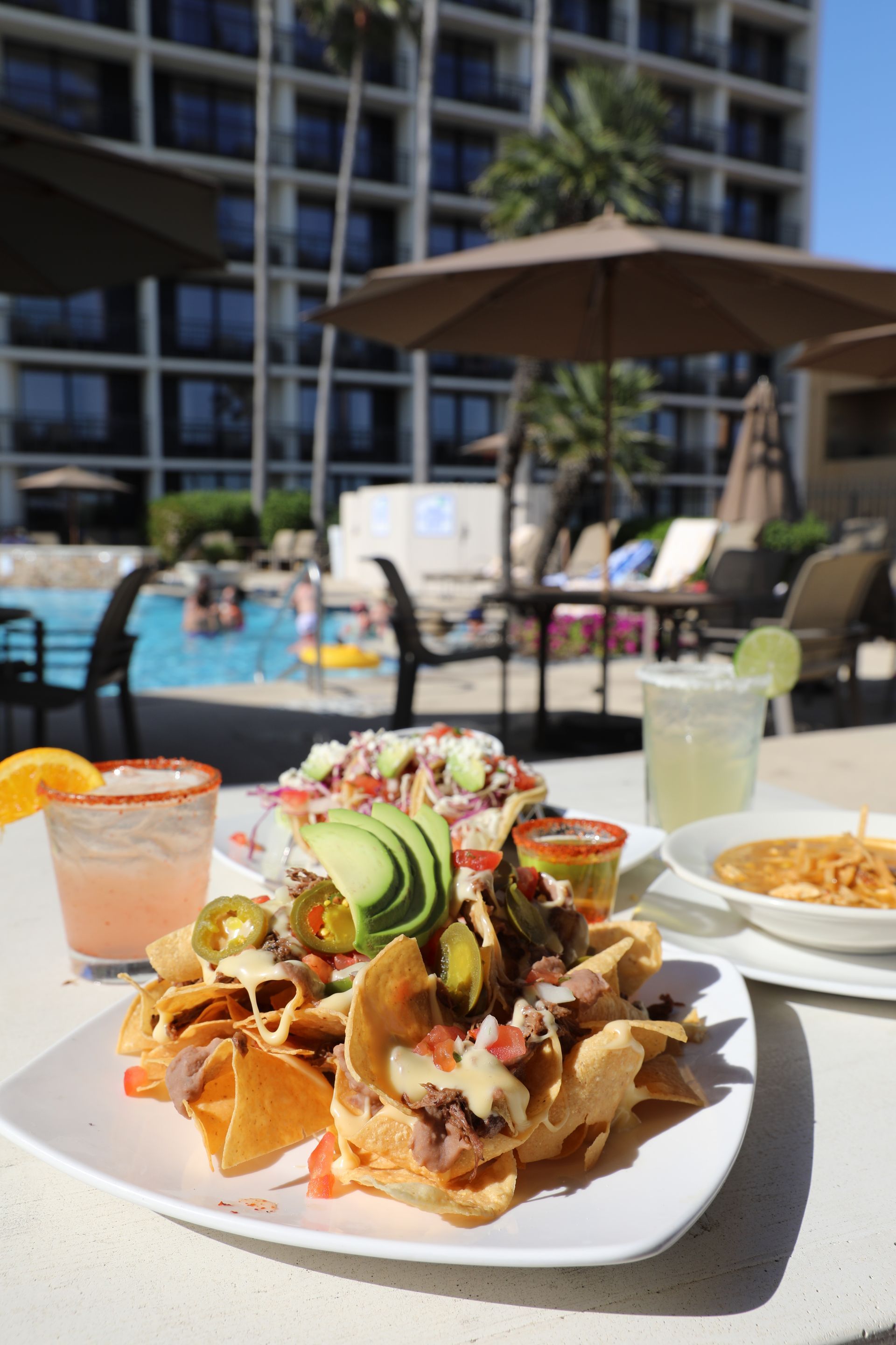 A plate of nachos and cocktails are sitting on a table next to a pool.