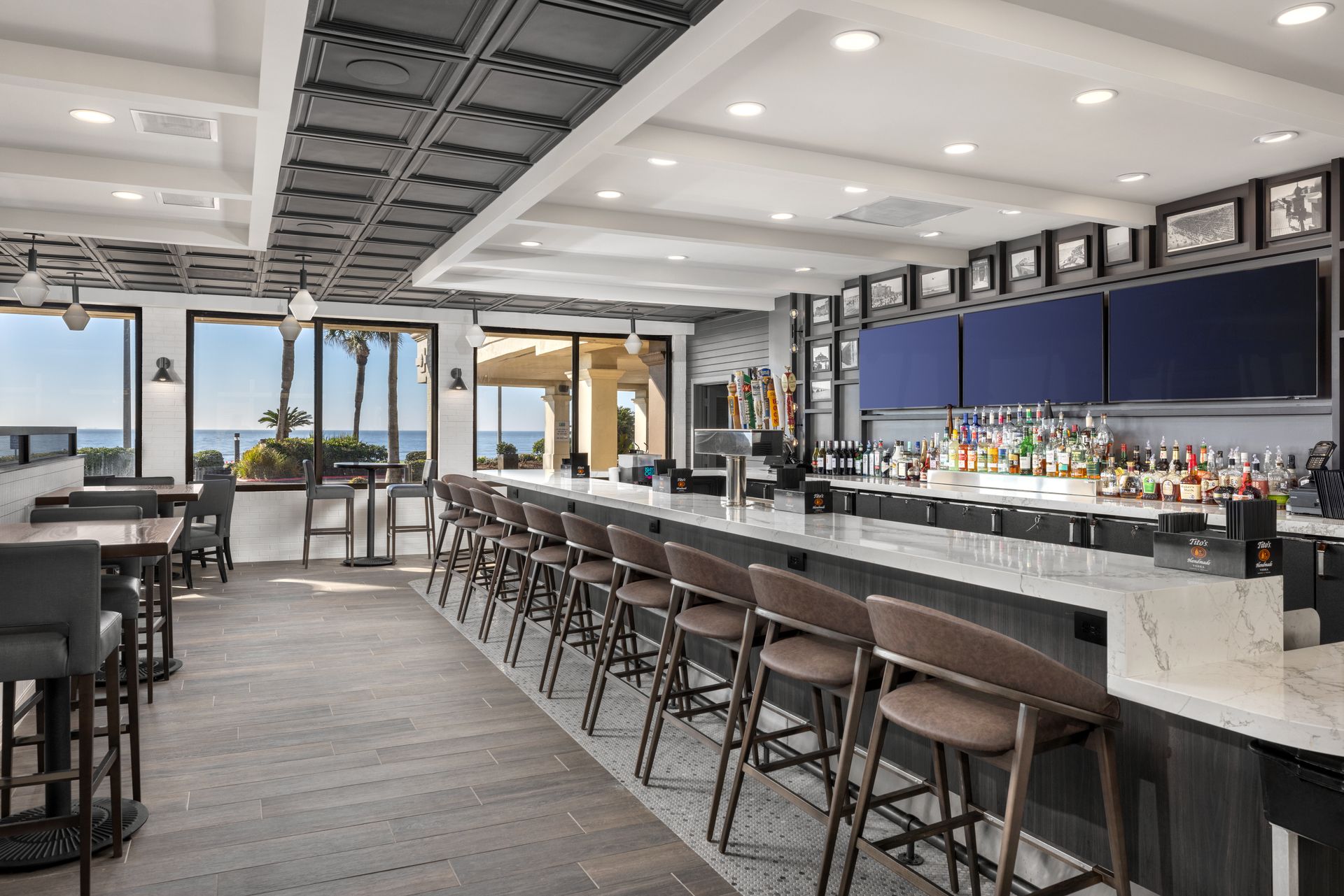 A long bar with a lot of chairs and tables in front of televisions in a restaurant.