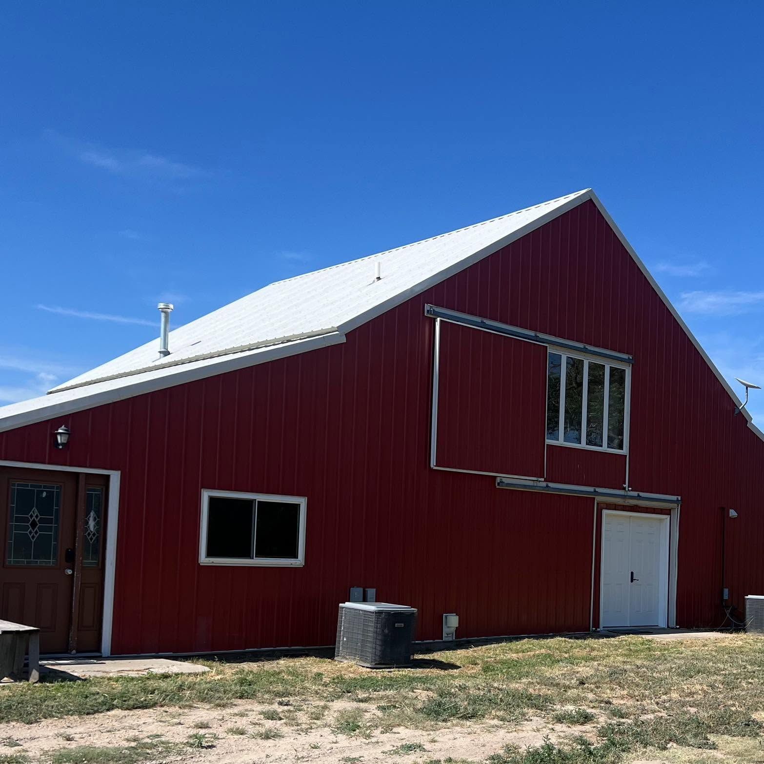 Red barn with white roof and large doors in a sunny rural field under a clear blue sky