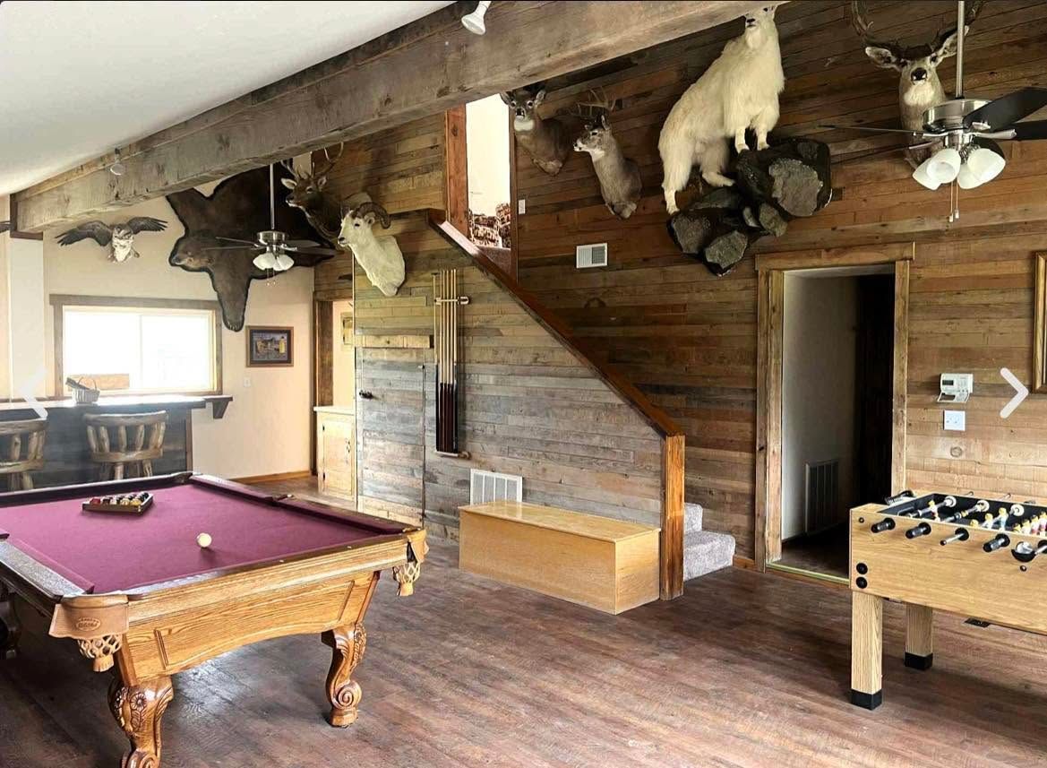 Rustic game room with pool table, foosball table, wooden stairs, and stone fireplace