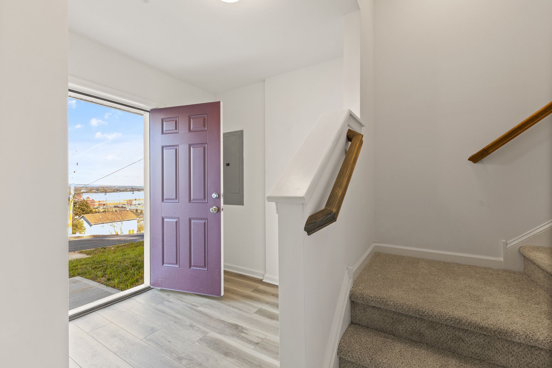 Open purple front door beside a carpeted stairway in a bright entry hall.