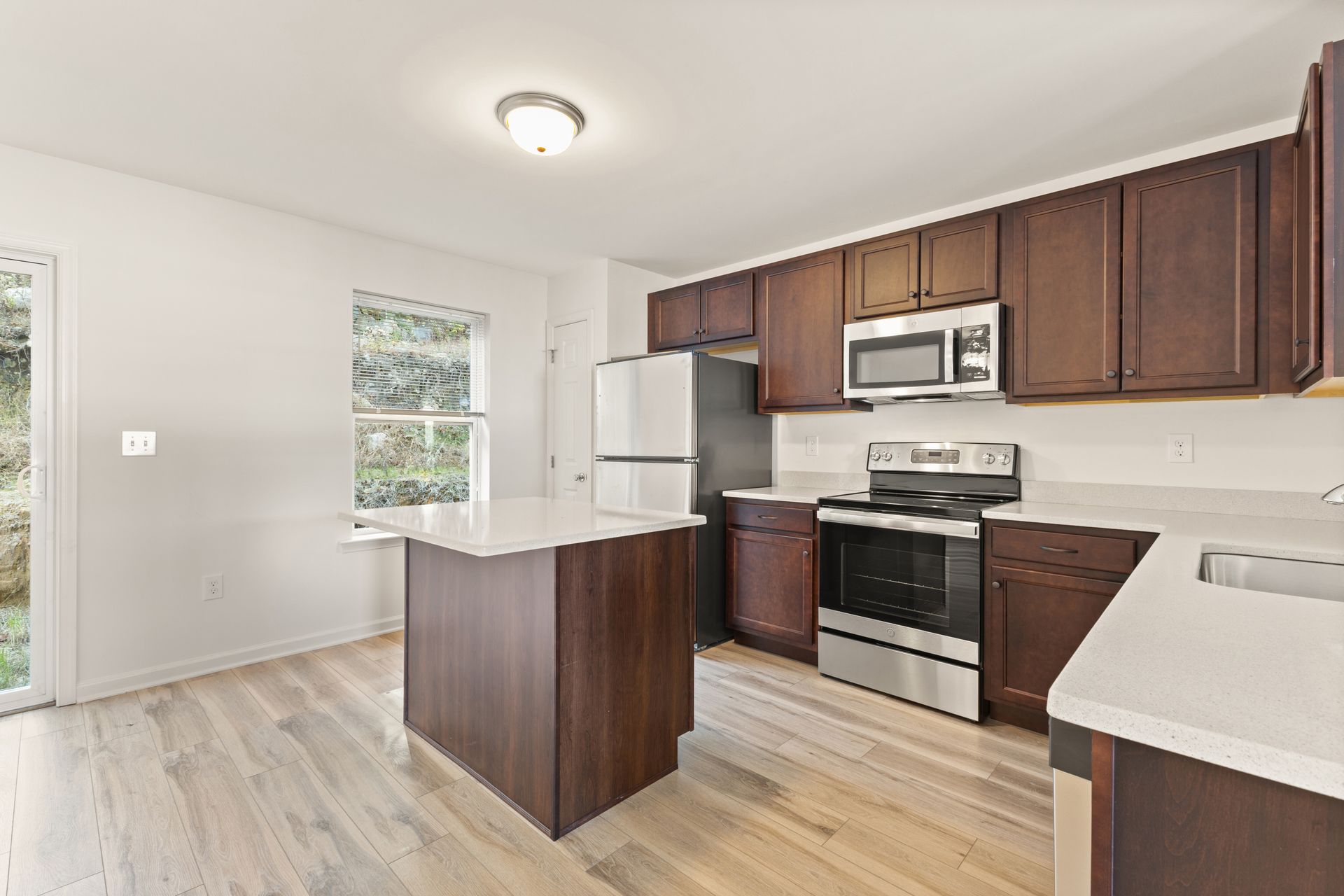 Bright modern kitchen with dark wood cabinets, white countertops, stainless appliances, and a center island.