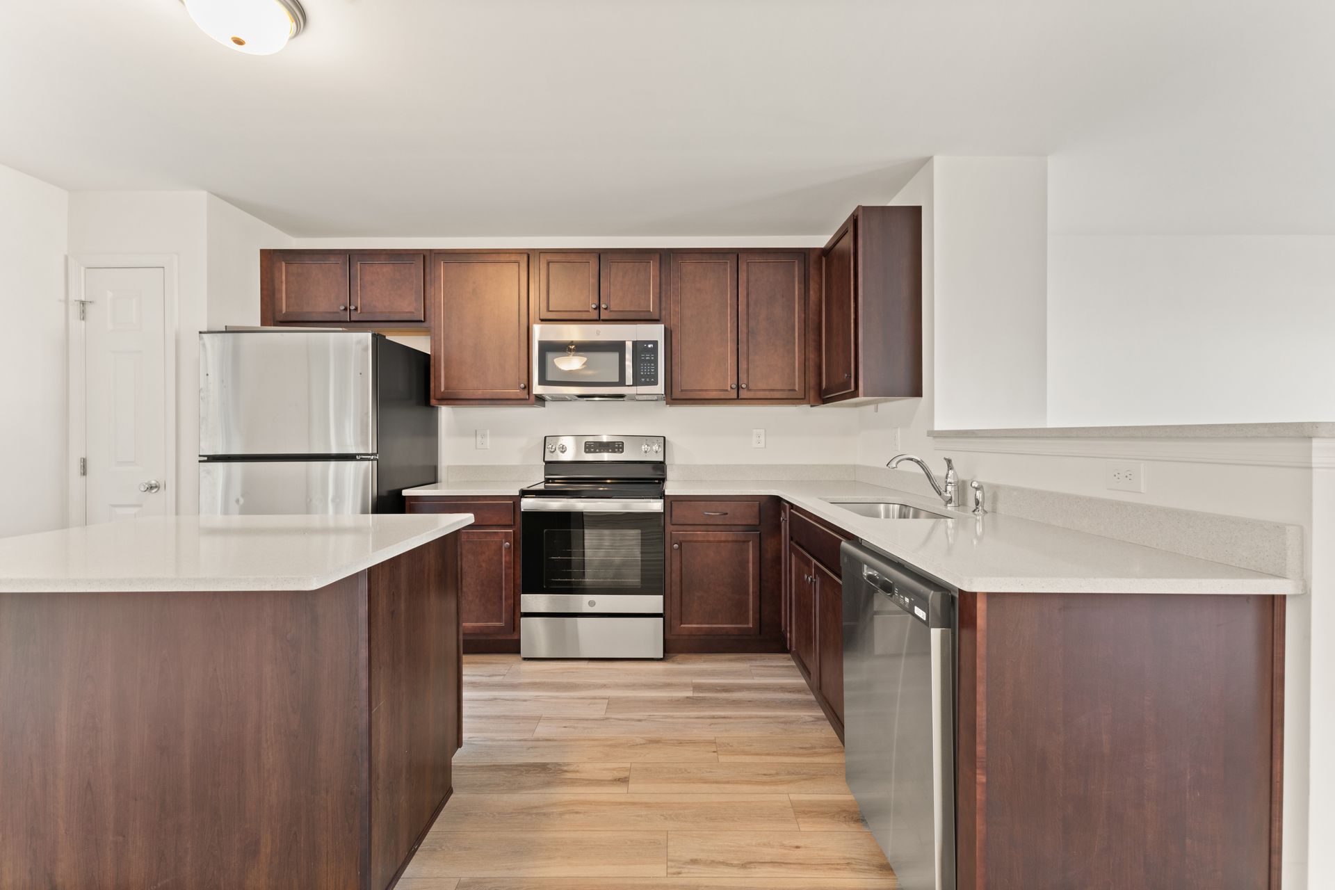 Modern kitchen with stainless steel appliances, dark wood cabinets, white countertops, and an island.