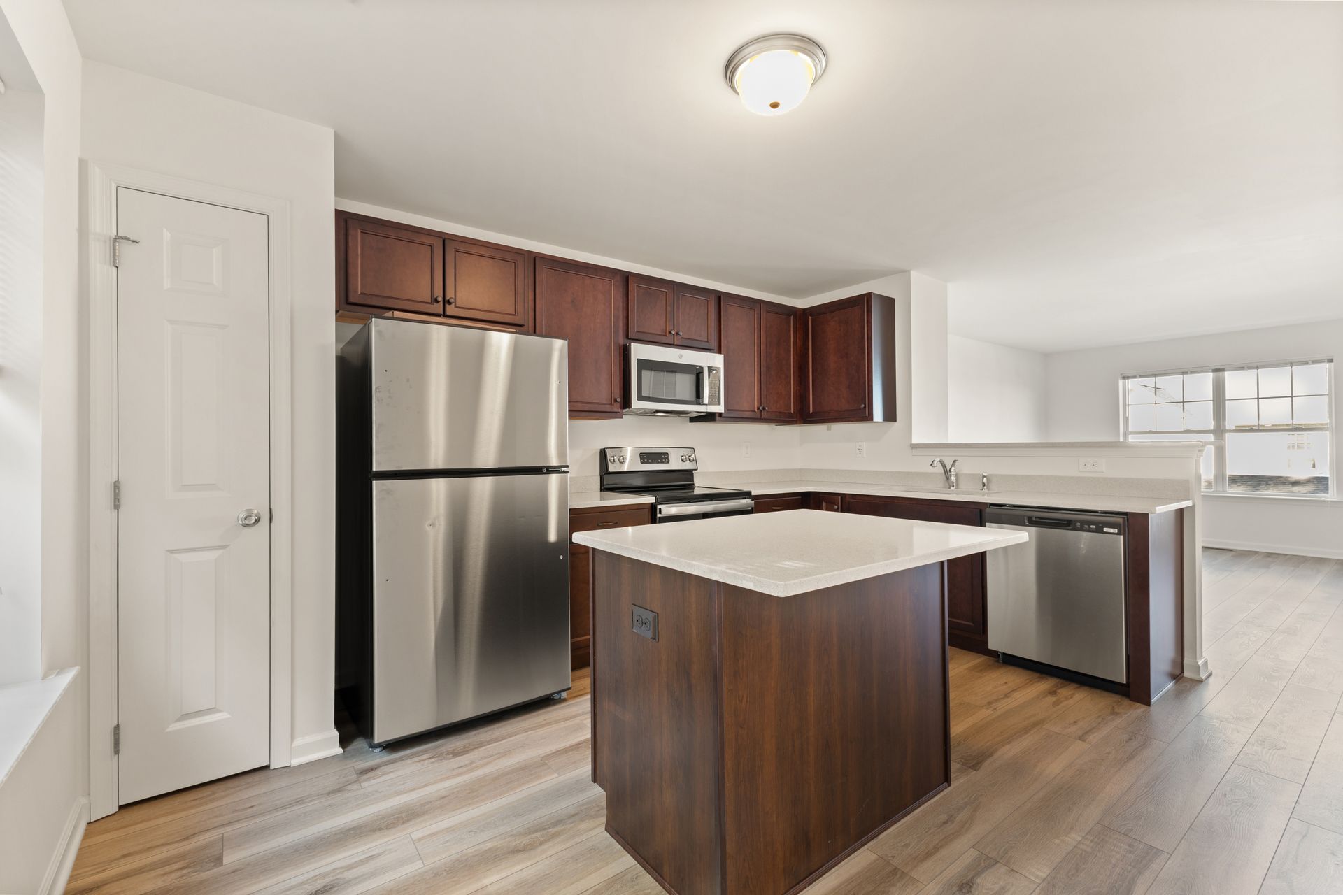 Modern kitchen with stainless steel appliances, dark wood cabinets, and a white island counter.