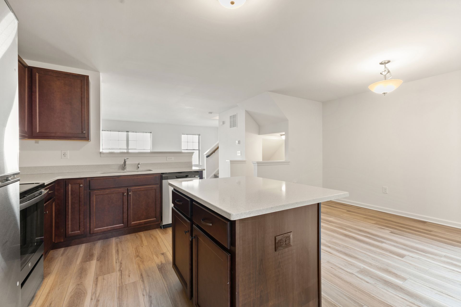 Empty kitchen and living area with white walls, dark wood cabinets, and a central island.