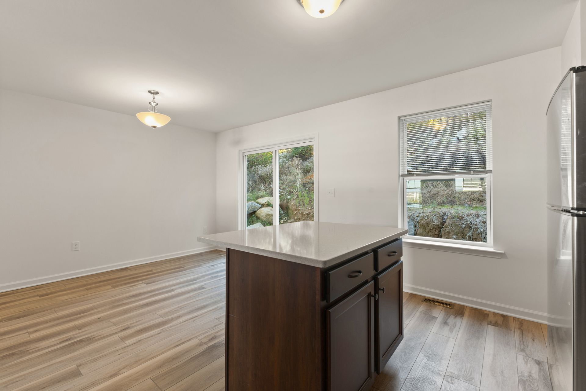 Empty bright kitchen with white walls, wood floors, and a dark island near windows.