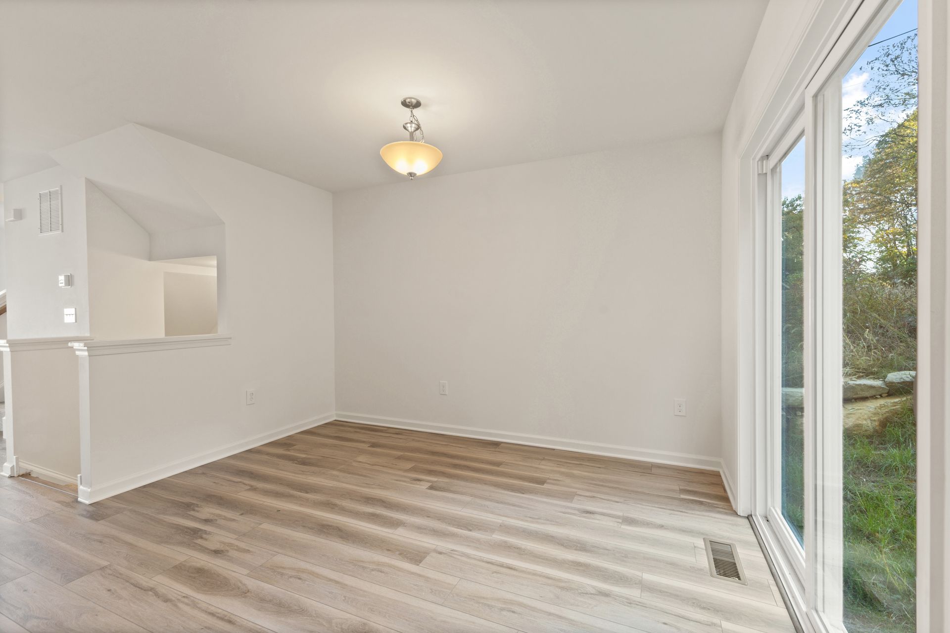 Empty bright living room with white walls, light wood flooring, and sliding glass doors.