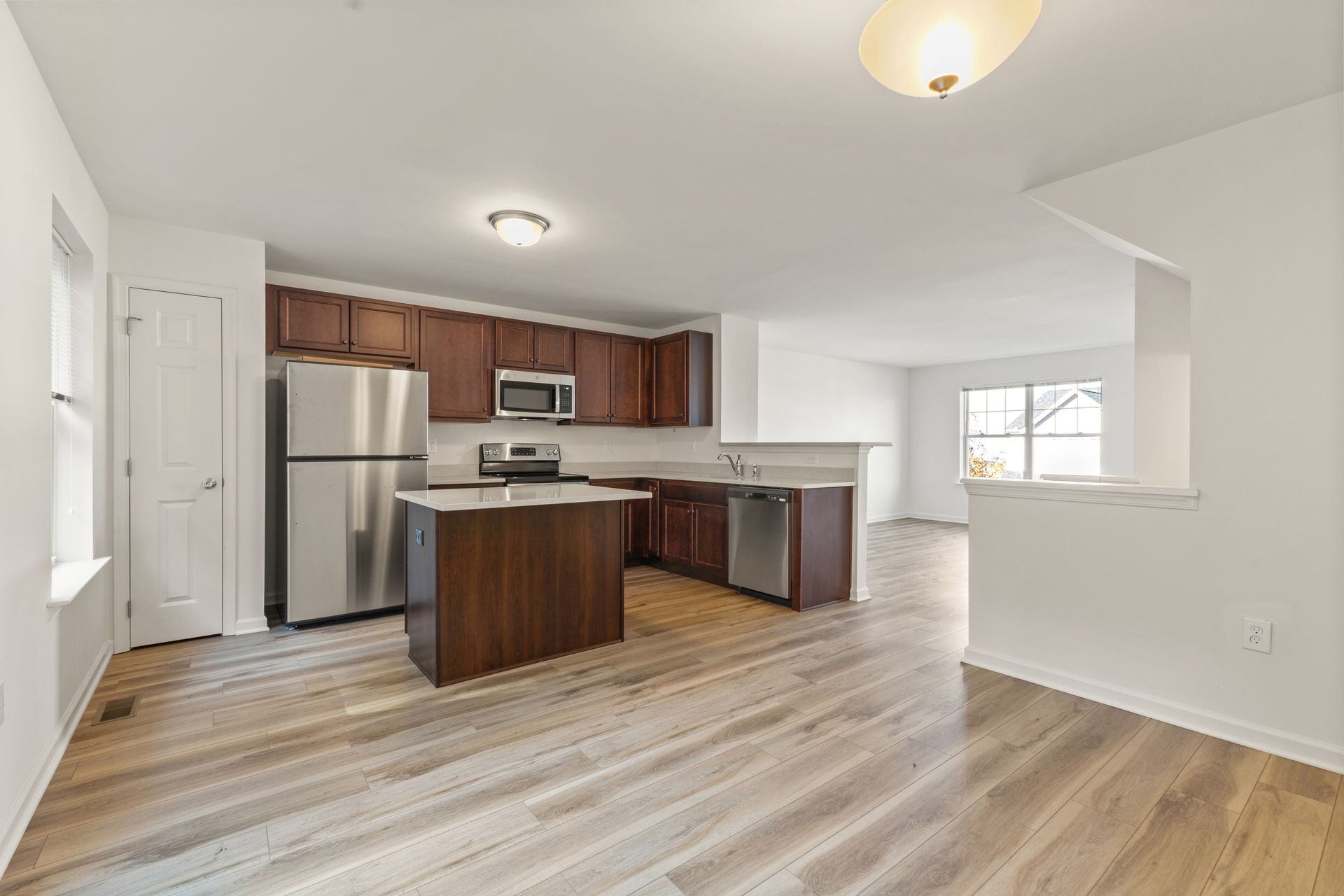 Open kitchen and dining area with stainless steel appliances, wood cabinets, and light wood flooring