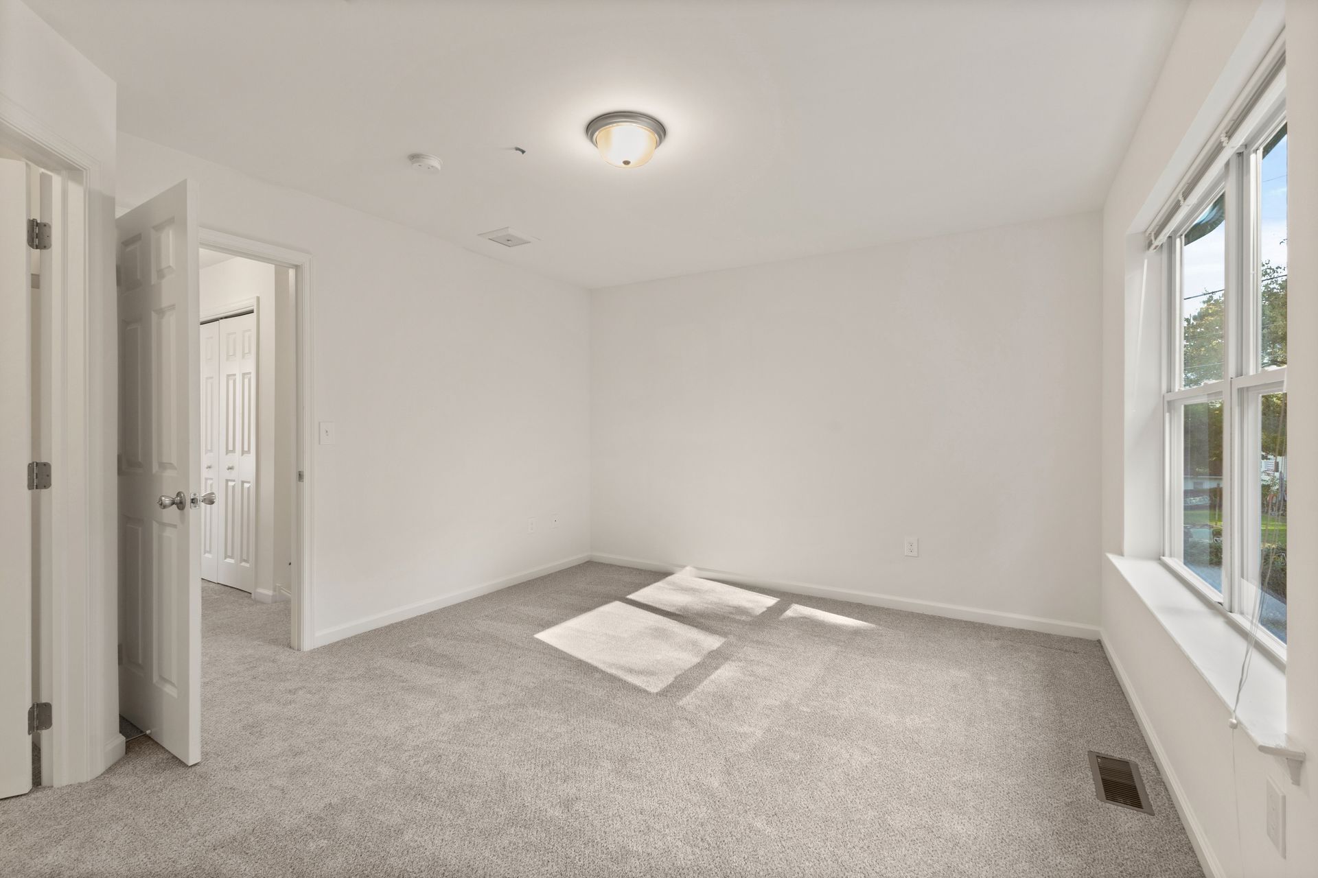 Empty white bedroom with gray carpet, two windows, and an open door to the hallway