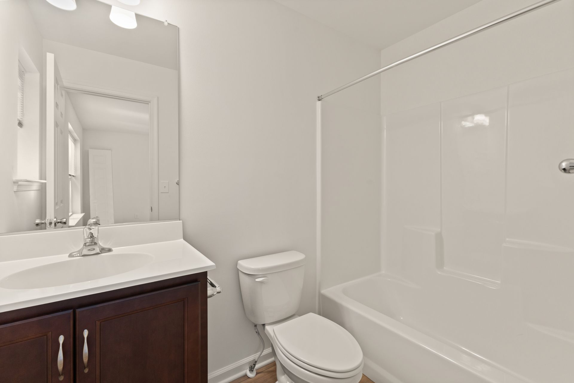 Small beige bathroom with vanity, mirror, toilet, and white tub-shower combo