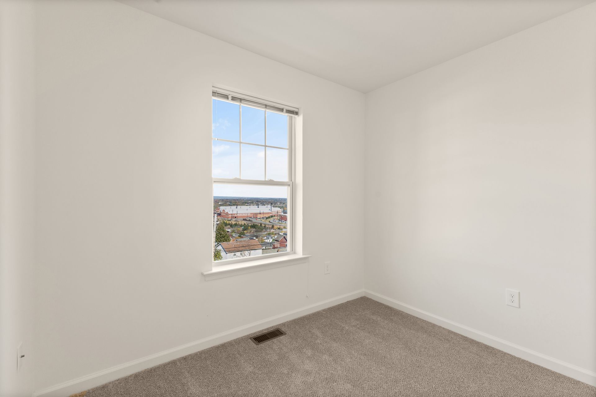 Empty white bedroom with carpet, a window, and a view outside.