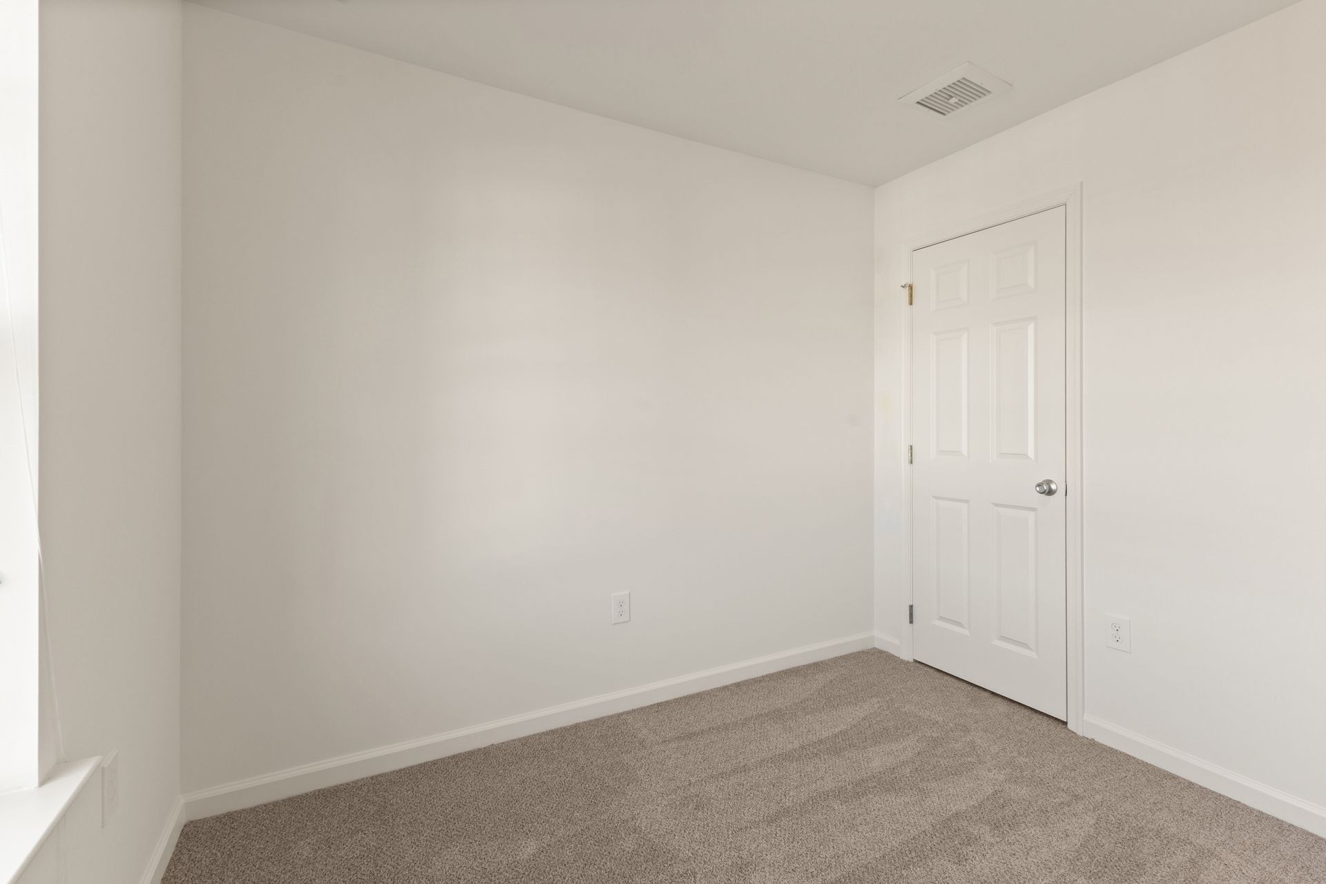 Empty white bedroom with beige carpet and a closed door