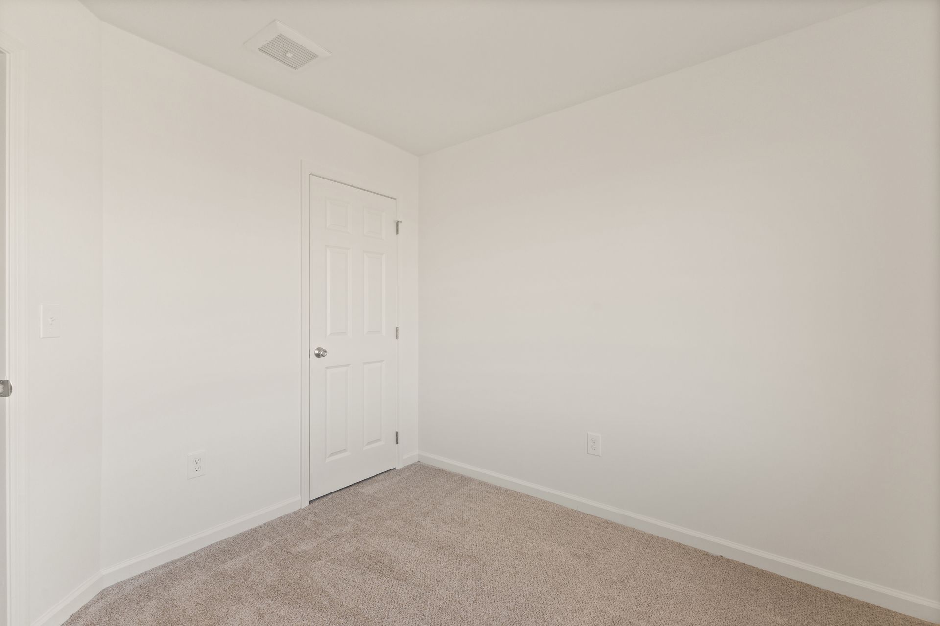 Empty white bedroom corner with beige carpet and a closed door