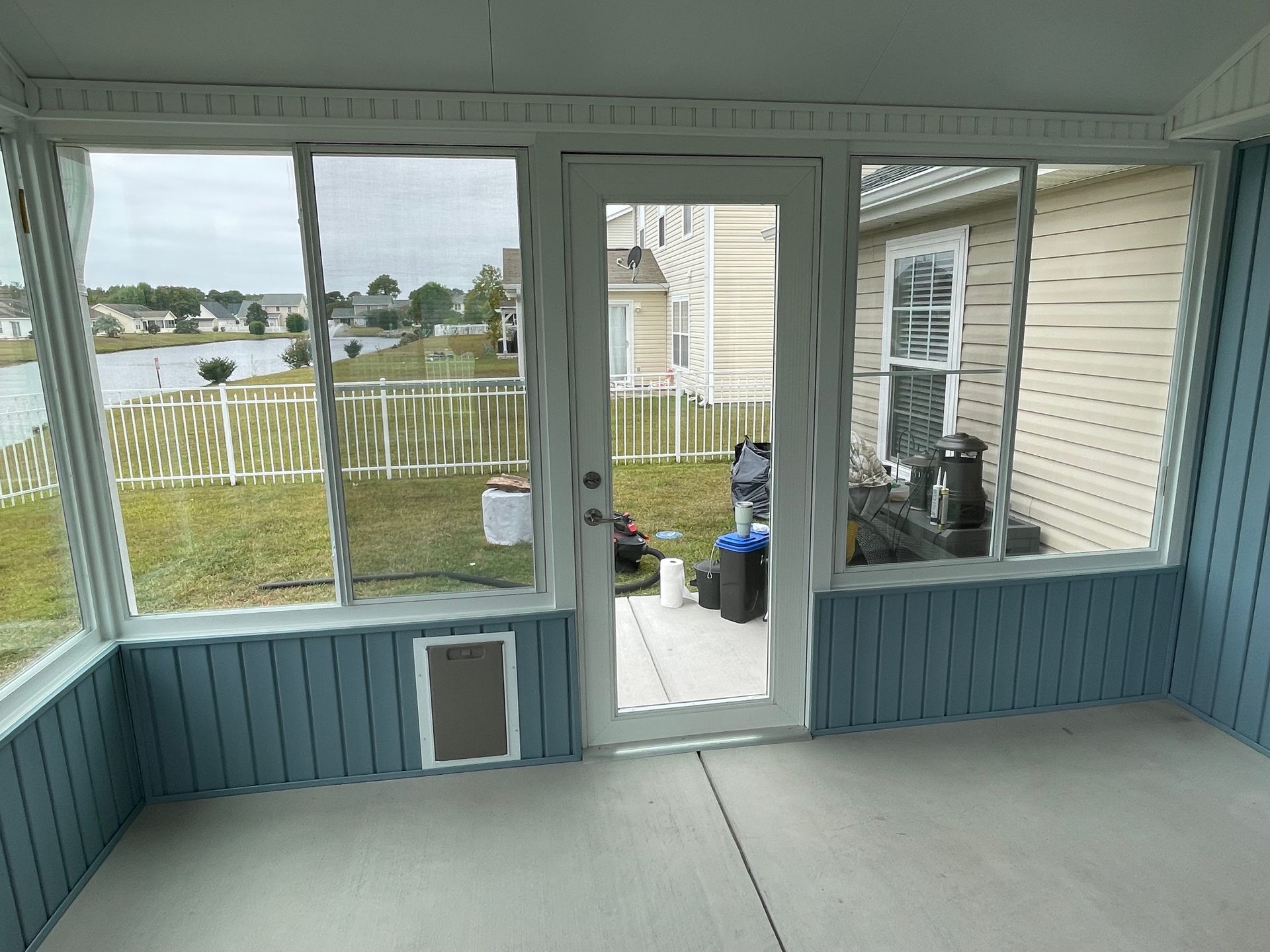 Screened-in porch with blue paneling, door, and windows overlooking a yard and water.
