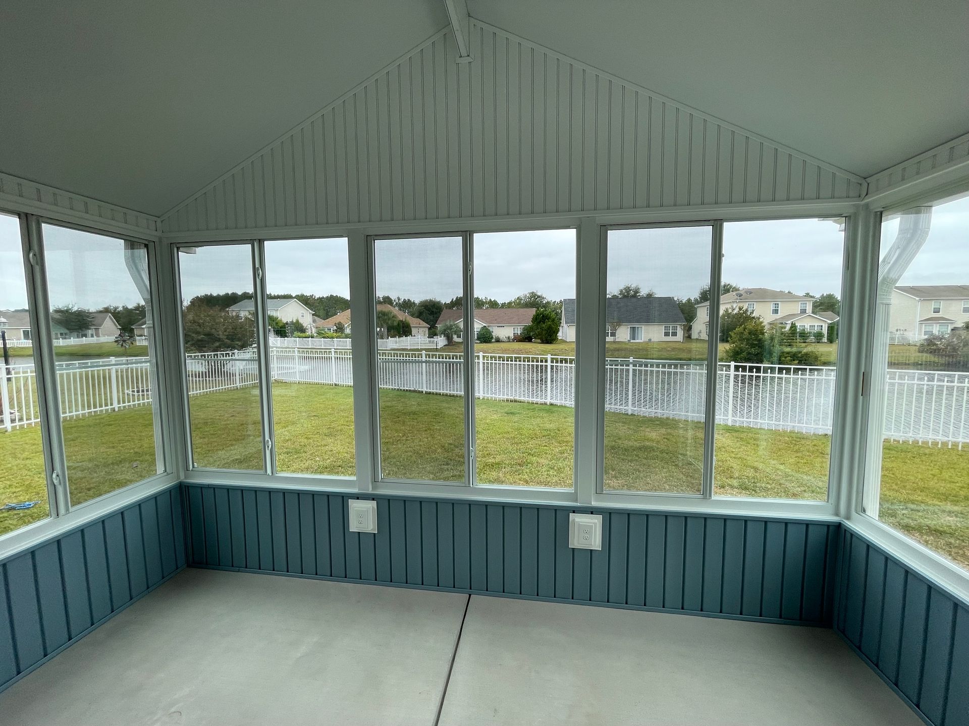 Screened porch overlooking a lake and houses, with blue paneling and white trim.