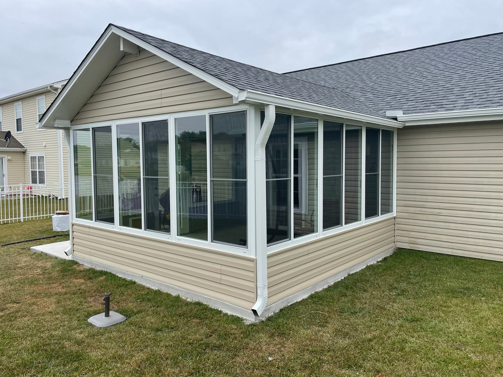 Beige screened-in porch with windows attached to a house with tan siding and a dark gray roof.