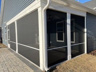 Screened-in porch with dark screens, white framing, and a brick patio. Gutters visible.