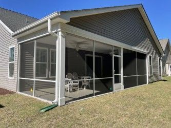 Screened porch attached to a house with white trim, gray siding, and outdoor furniture.