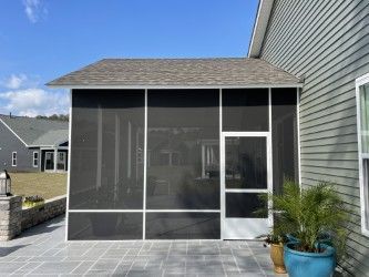 Screened-in porch attached to a house with gray siding. Porch has a gray roof and tiled floor.