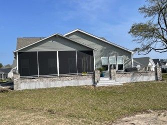 A house with a screened porch and a brick foundation under a clear blue sky.