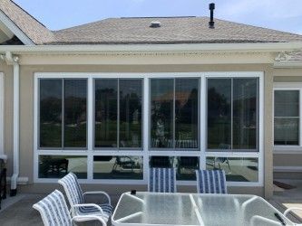 Sunroom with large windows, white frames, beige exterior, and outdoor furniture.