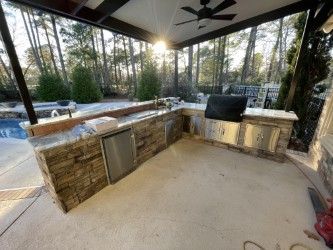 Outdoor kitchen with a grill, refrigerator, and sink. Built-in stone countertops and cabinetry.