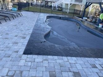 A pool surrounded by gray paving stones and a dark border, next to a brick patio.